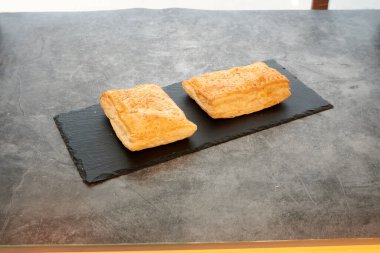 Siyah tabakta iki parça hamur işi. Tabak tezgahın üzerinde. Pasta altın kahverengidir.