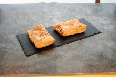 Siyah tabakta iki hamur işi. Biri şekerle kaplı. Diğeri ise değil. Tabak tezgahın üstünde.