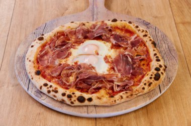 Jambonlu ve yumurtalı bir pizza. Pizza tahta bir tahtanın üzerinde. Pizza kahverengi ve bir sürü peyniri var.