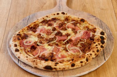 Jambonlu ve soğanlı bir pizza. Tahta bir tahtanın üzerinde duruyor. Pizza kahverengi ve çıtır çıtır.