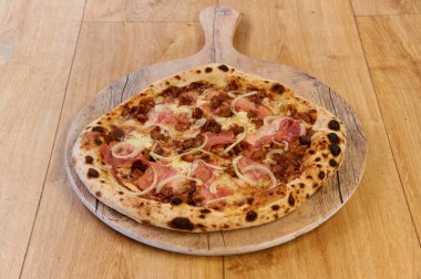 Tahtada jambonlu ve soğanlı bir pizza. Pizza kahverengi ve kabuklu.