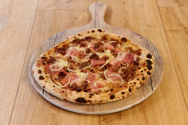 Tahtada jambonlu ve soğanlı bir pizza. Pizza kahverengi ve kabuklu.