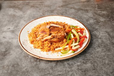 Bir tabak et ve sebzeyle birlikte bir tabak yemek. Tabak masanın üstünde. Et kahverengidir, sebze yeşildir.