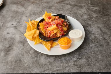 Siyah tavalı ve beyaz tabaklı bir tabak yemek. Tabakta bir kase yiyecek ve patates kızartması var.