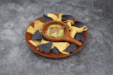 Bir tabak tortilla cipsi ve bir kase guacamole. Kase tabağın ortasında ve cipsler etrafa saçılmış.