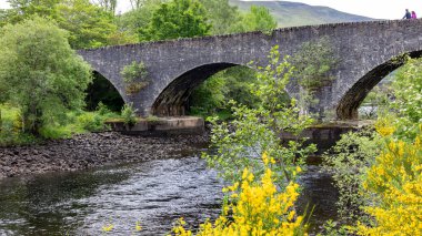 RIVER TÜMMEL, PERTHSHIRE, SCOTLAND, İngiltere, 25 MAYIS. 25 Mayıs 2024 'te İskoçya' nın Perthshire kentindeki Tummel Nehri üzerindeki eski taş köprü. Kimliği belirsiz iki kişi.