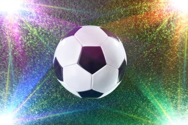 Köşelerden aydınlatan renkli spot ışıklarıyla çimlerin üzerinde klasik futbol topu. Üst görünüm.