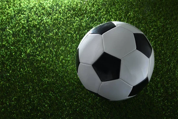 Classic soccer ball on synthetic grass illuminated by a spotlight. Top view. Horizontal composition.