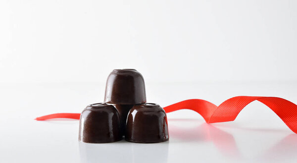Stacked chocolate bonbons with red bow on white table isolated with white background. Front view.