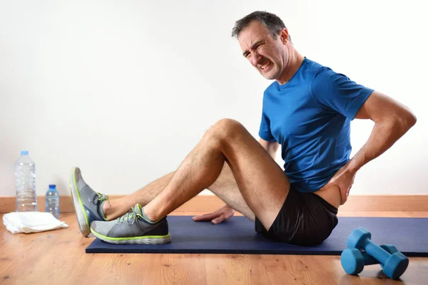 男は畳の上に座って腰の痛みを屋内で不平を言うスポーツをしている サイドビュー — ストック写真