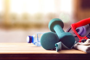 İki dambıl havlusu ve bir şişe suyla ahşap masada spor aletleri. Ön görünüm.