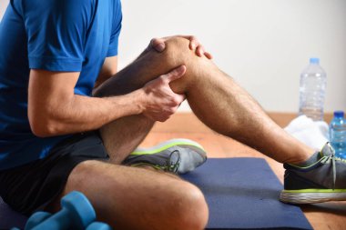 Detail of man doing sports with knee pain holding himself with his hand sitting on a mat. Side view. clipart