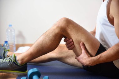 Detail of man doing sports with hamstrings pain holding himself with his hand sitting on a mat. Side view