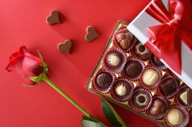 Romantic gift of a box of chocolates with a red rose on a red background. Top view.