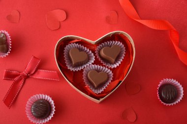 Chocolates in heart shaped box on red table decorated with hearts and red ribbons. Top view.
