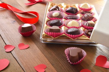 Presentation of assortment of chocolates with red heart-shaped cutouts on wooden table. Elevated view.