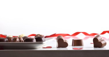Assortment of chocolates served on a plate on a white table with several heart-shaped chocolates and a white isolated background. Front view.