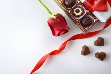 Basic background with box of chocolates on white table with a red rose. Top view.