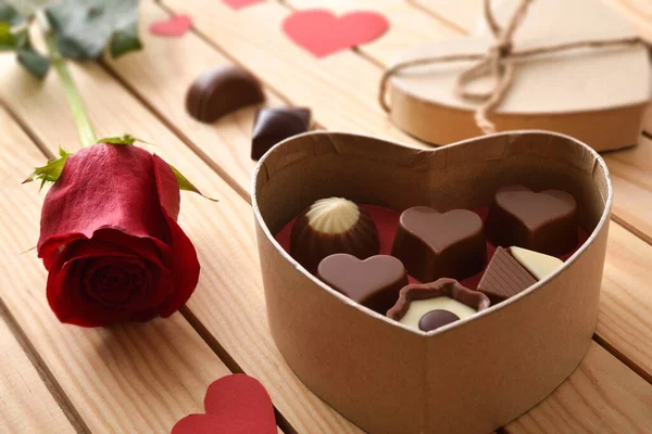 Box with assorted chocolates and red rose on wooden slatted table. Elevated view.