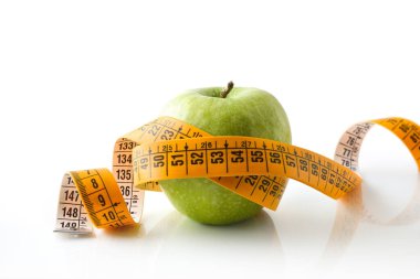 Apple and tape measure crossed around reflected on white base and white isolated background. Healthy life style.. Front view.