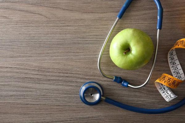 Health check and healthy lifestyle with apple, tape measure and stethoscope on wooden table. Top view.