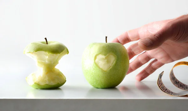 Action of eating apples for health with hand picking apple with heart with half eaten apple and measuring tape with white isolated background. Front view.