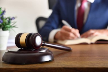 Detail of gavel and lawyer dressed in the toga signing a document on wooden table. Front view