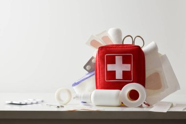 Travel portable first aid bag full of objects and tools for minor cures on white table. Front view. Horizontal composition