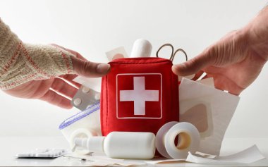 First aid kit concept with hands picking up bag full of tools and medicine on white isolated background. Front view. Horizontal composition.