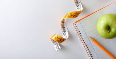 Health plan with pencil and apple on notebook on white table with tape measure. Top view.