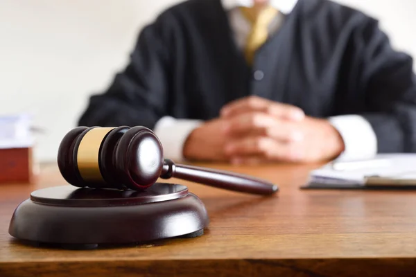 Detail of gavel and judge dressed in the toga sitting in the background on wooden table. Front view
