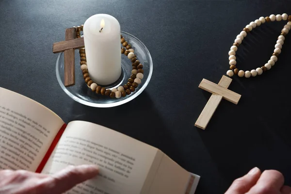 Christian believer reading bible on black nightstand with religious items for prayer with christian cross open bible and lighted candle on glass plate