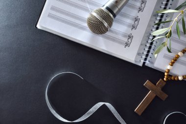 Palm Sunday için koro müziği notaları, mikrofon ve siyah bir masada Hristiyan haçı olan zeytin dalları. Üst görünüm.