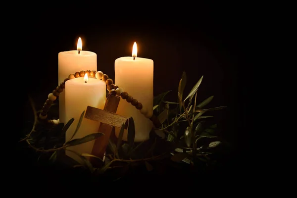Easter religious background with three burning candles illuminating christian cross and olive branches around in the twilight. Front view.