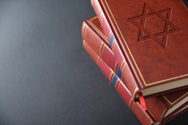 Стопка книг с коричневой кожаной обложкой с выгравированным символом еврейской культуры и религии на черном столе. Повышенный вид.