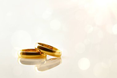 İki altın yüzüğün ayrıntıları, biri diğerinin üstünde Bokeh 'in altın arka planına sahip cilalı bir zemine yansıyor. Ön görünüm.