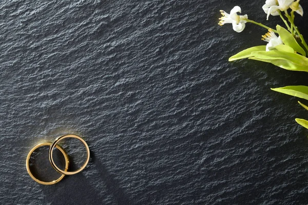 1つのコーナーで2つの金のリングと別の花との結婚発表のための石の背景をスレート トップ表示 — ストック写真