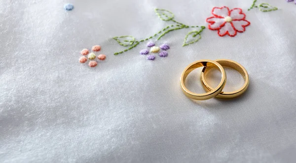 2つの金の結婚指輪の詳細は 花の刺繍と白い布の上に互いに横たわっている 上からの眺め — ストック写真