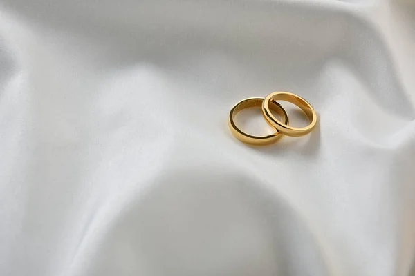Detail of two elegant gold rings on white shiny fabric. Top elevated view.