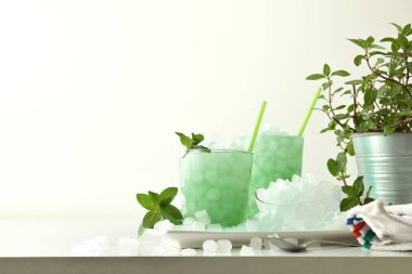 İki bardak nane şekeri tabakta, içi buz dolu ve beyaz masada nane bitkisi ve izole bir arka plan. Ön manzara. Yatay bileşim.