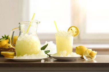 Sürahide buzlu limonata ve ahşap bir bankta cam meyveli ve arka planda güneşli bir pencere olan ezilmiş buzlu bir buz. Ön manzara. Yatay bileşim.