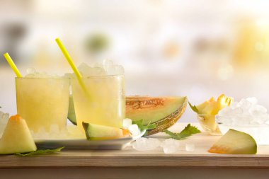 İki bardak buzlu karpuz içeceği ezilmiş buz dolu ahşap masa ve arka planda mutfak olan dilimlenmiş meyve. Ön manzara. Yatay bileşim.