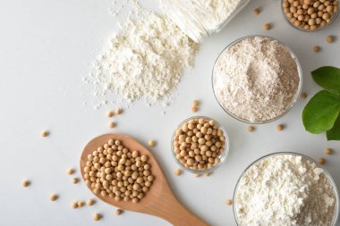 Tam ve rafine soya unu, cam kaselerde soya fasulyesi ve beyaz masada ahşap kepçe. Üst görünüm.