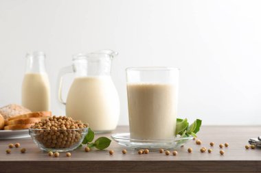 Alternatif kahvaltı için soya içecekleriyle dolu cam kaseler, ahşap masa üzerinde soya fasulyesi dolu, hamur işleri ve beyaz izole edilmiş arka plan. Ön görünüm.
