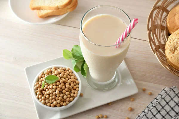 Soy drink in tall glass with soy beans in container on wooden bench in a kitchen. Elevated view.