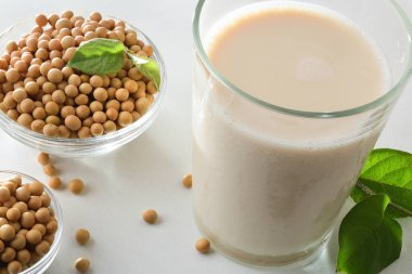 Soya alternatif içeceği bardakta beyaz masada, içi kuru tohumlarla dolu. Yüksek görünüm.