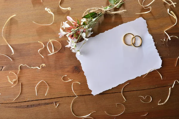 木のテーブルの花が付いている白いペーパー カードの2つのリングはまわりで回ります トップビュー — ストック写真