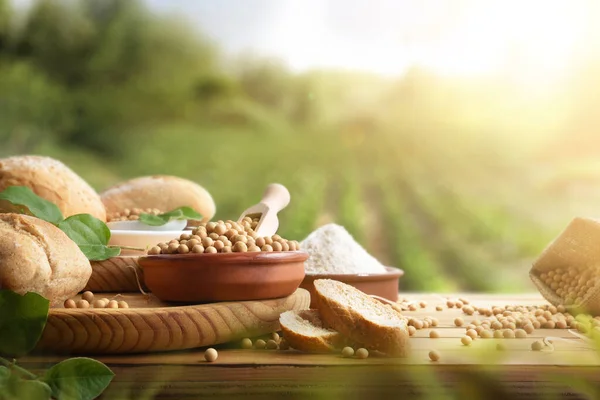 Table with soy products, such as bread and flour in the countryside with harvest in the background. Front view.