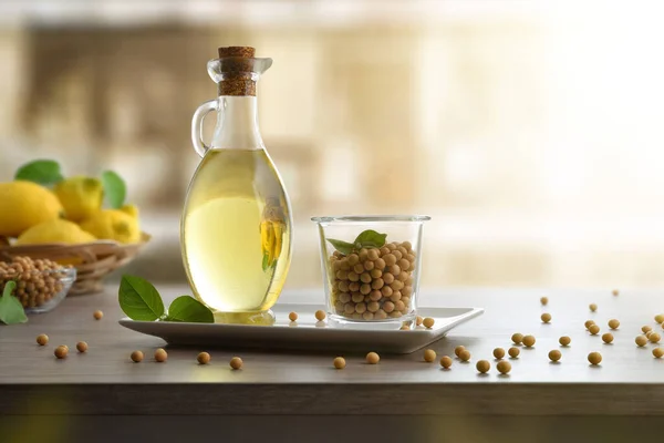 Soybean oil in glass with dry soy beans in white plate on wooden table and white isolated background. Font view.