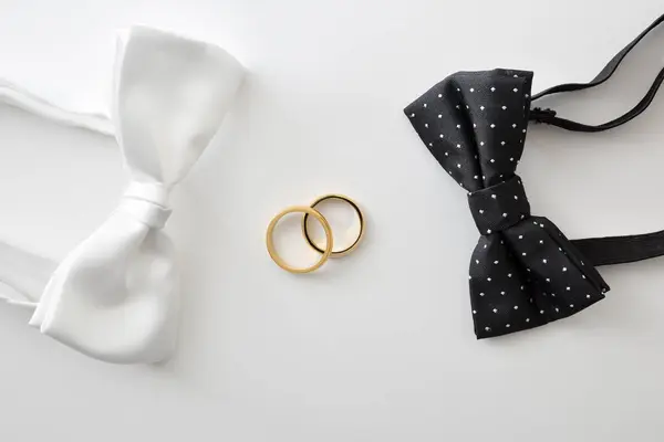 Gay wedding concept with black bow tie with polka dots and white on the sides of wedding rings in the center. Top view.